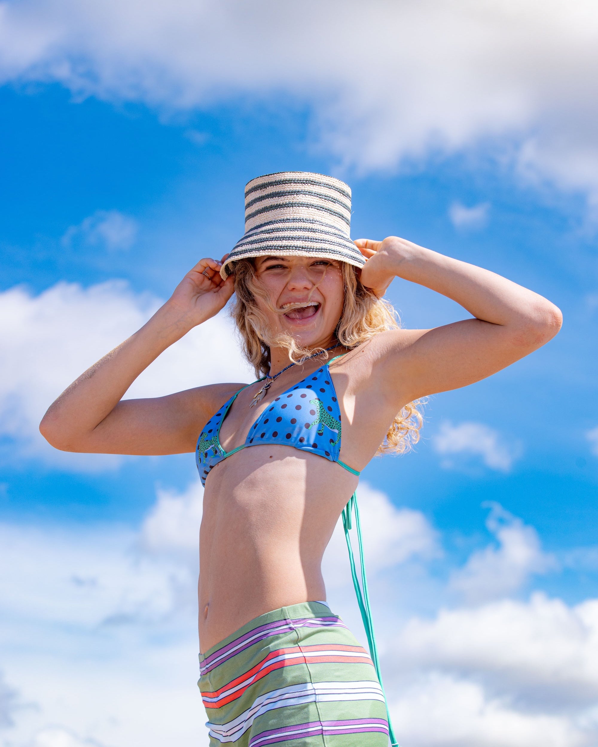 Woman in a colorful bikini and striped straw bucket hat against a blue sky with clouds