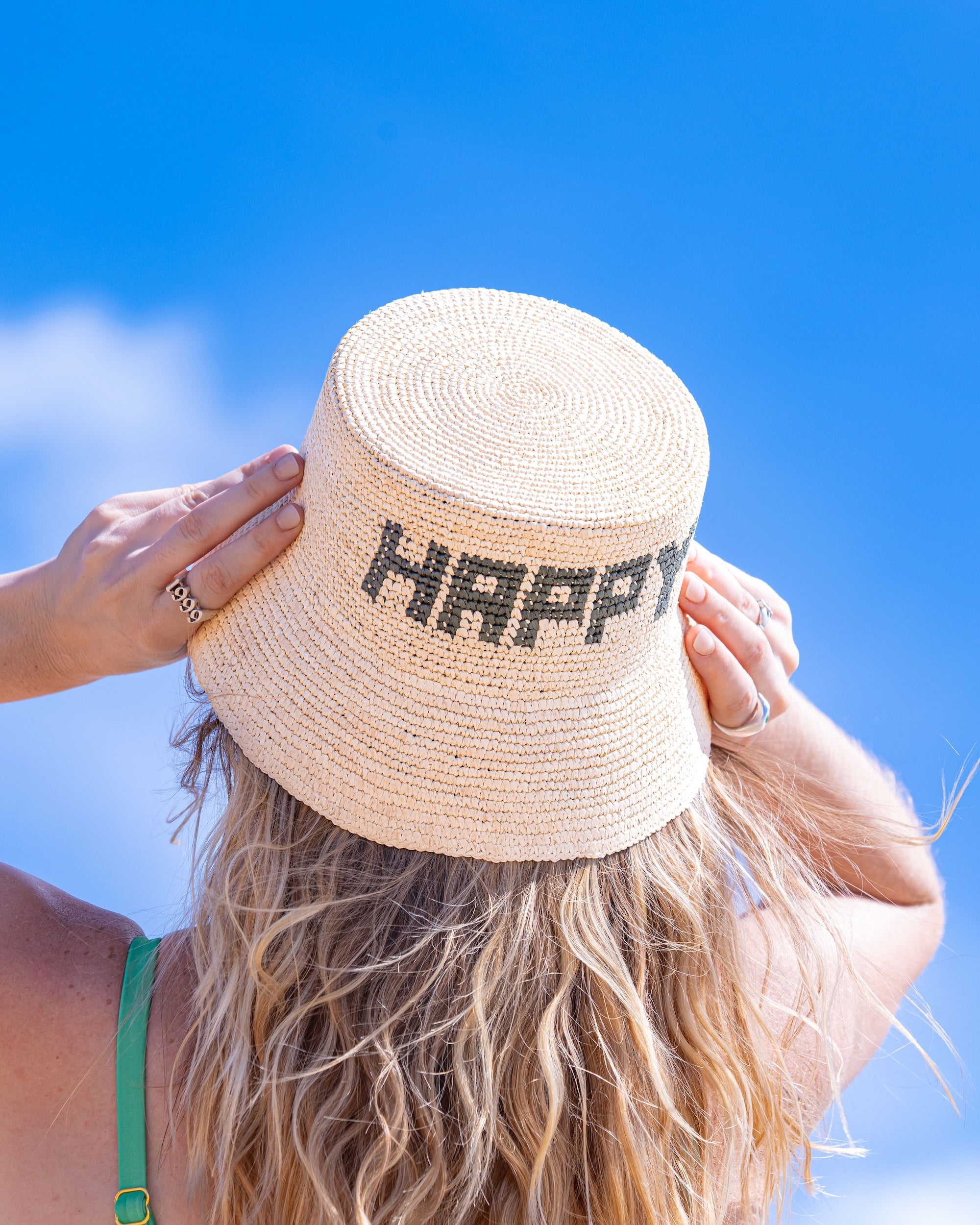 Person wearing a straw hat with 'HAPPY' text against a blue sky