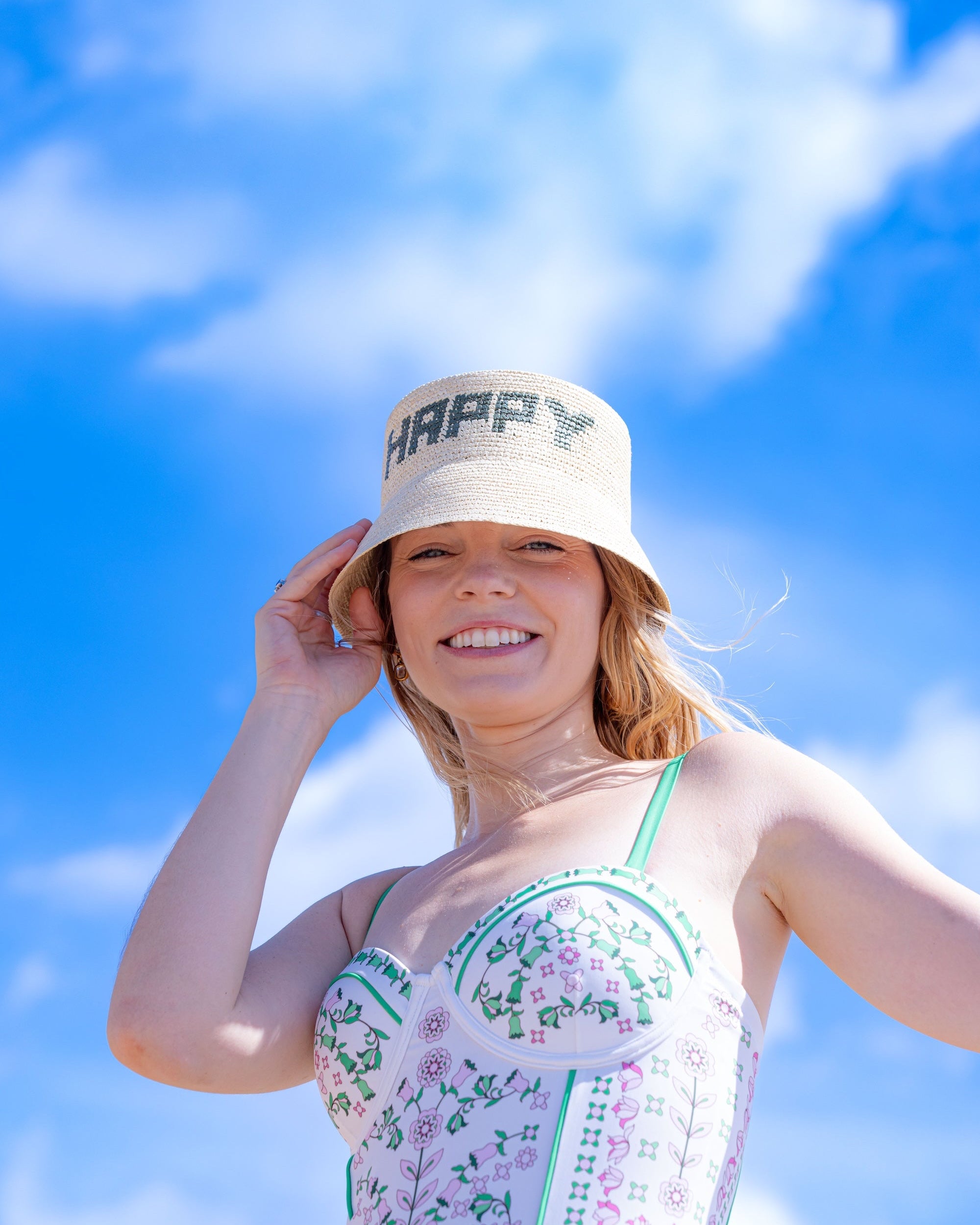 Woman wearing a 'Happy' bucket hat against a blue sky