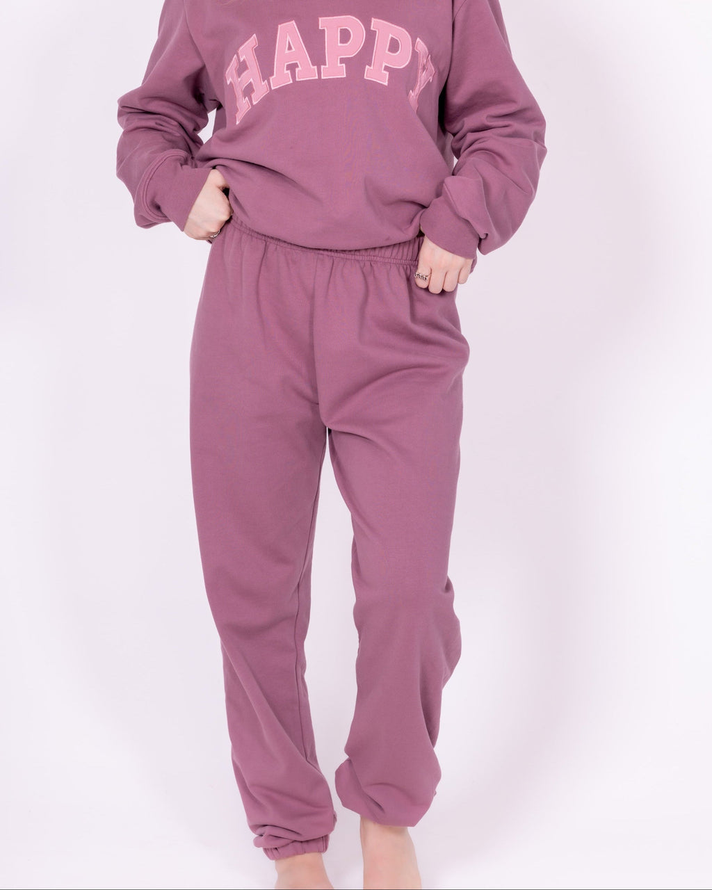 Person wearing a mauve 'HAPPY' sweatshirt and pants on a white background